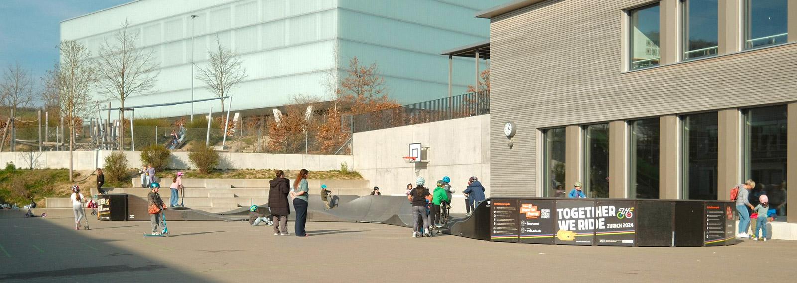 Kincer spielen und üben sich im Fahren auf  dem mobilen Pumptrack mit ihren Kickboards und Velos.