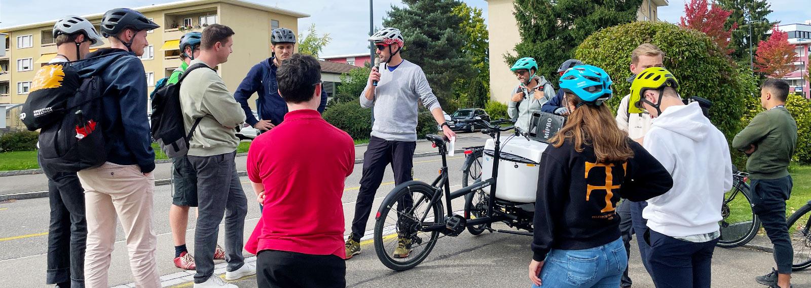 Studierende der Fachhocschule OST stehen auf einem Vorplatz in Uster um ein Lastenvelo herum und lauschen den Ausführungen unseres Dozenten.