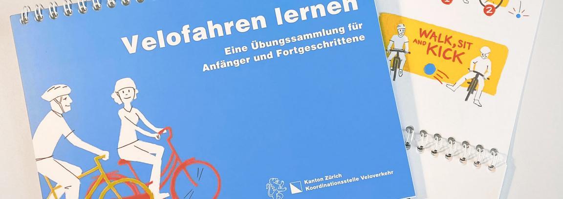 Zwei Übungsbüchlein zum Velofahren, das vordere zeigt das blaue Cover mit dem Titel «Velofahren lernen» und das hintere zeigt eine Illustration aus dem Inhalt.