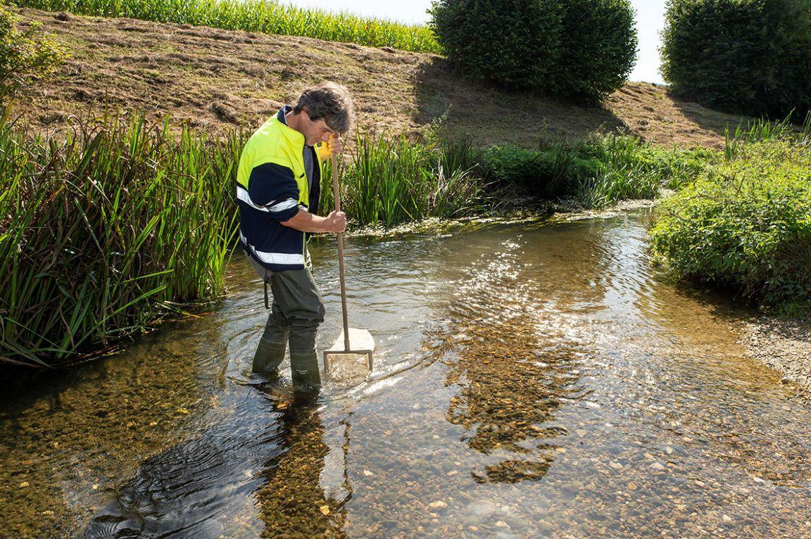 Mann mit gelber Leuchtwest stehend im Furtbach bei einer Probenahme zur Beurteilung des Zustands der wirbellosen Kleintiere (Makroinvertebraten) im Furtbach