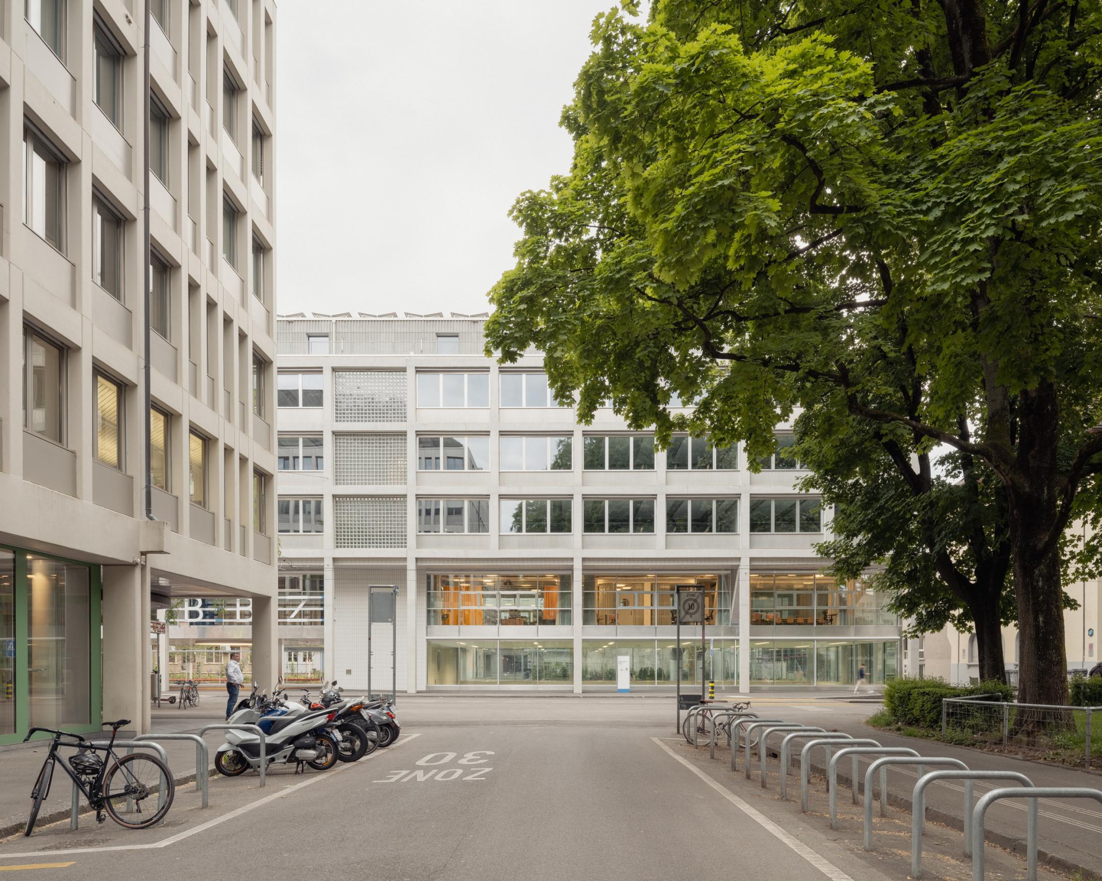 Strassenansicht mit Velos und Rollern im Vordergrund, im Hintergrund die BBZ mit einer Glasfassade mit vielen Fenstern.