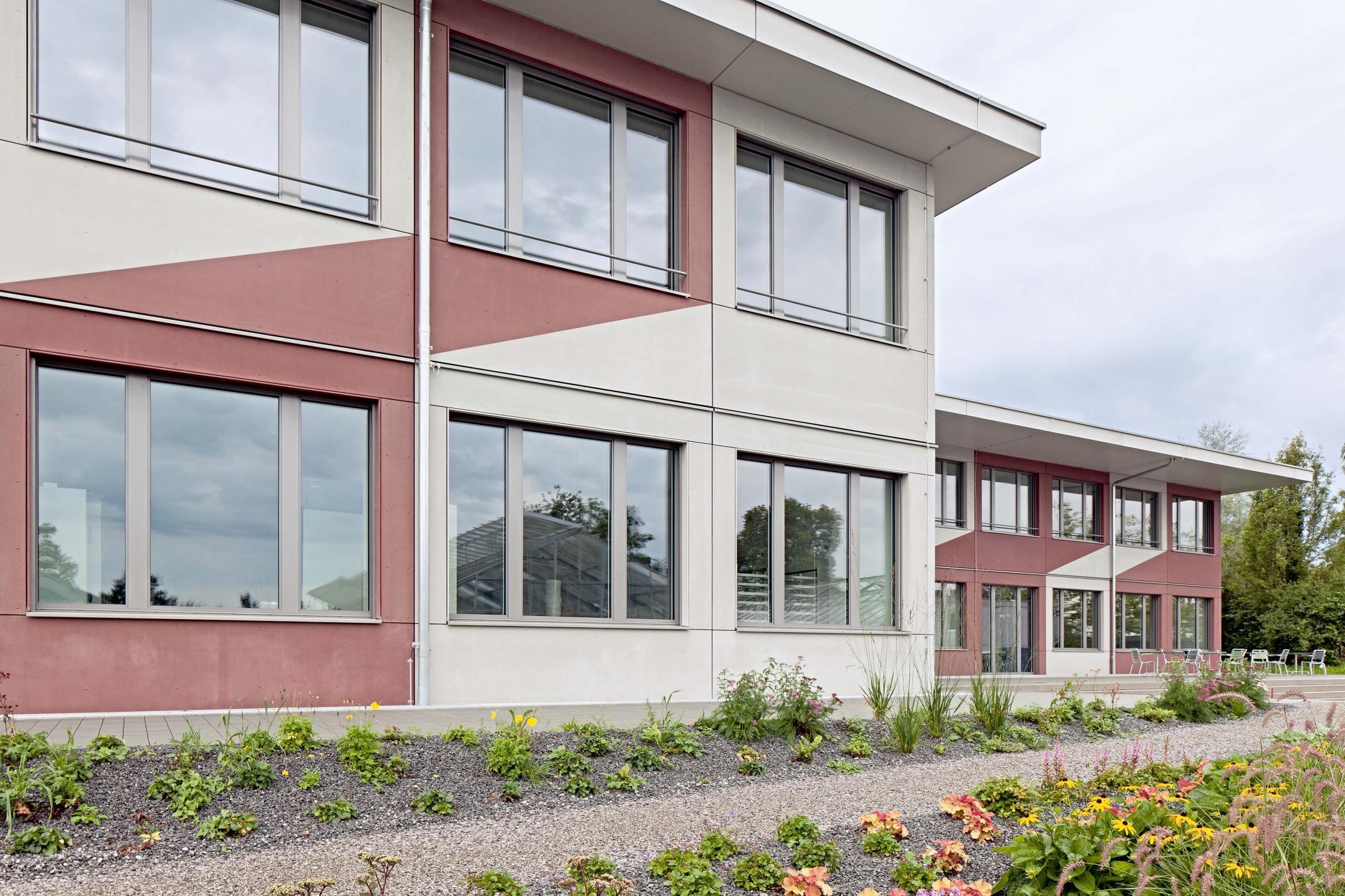 Fassadenansicht mit bescheidener Begrünung und Kiesweg im Vordergrund.