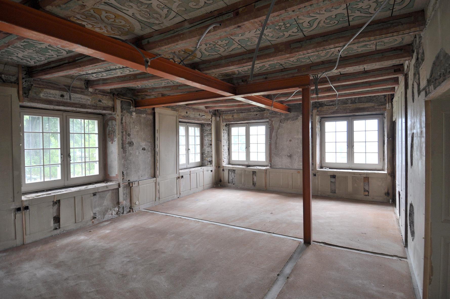 Zimmer im Erdgeschoss mit freigelegten originalen Decken- und Wandmalereien aus der Barockzeit. Die Decken werden noch mit orangen Stützen aufrecht gehalten.