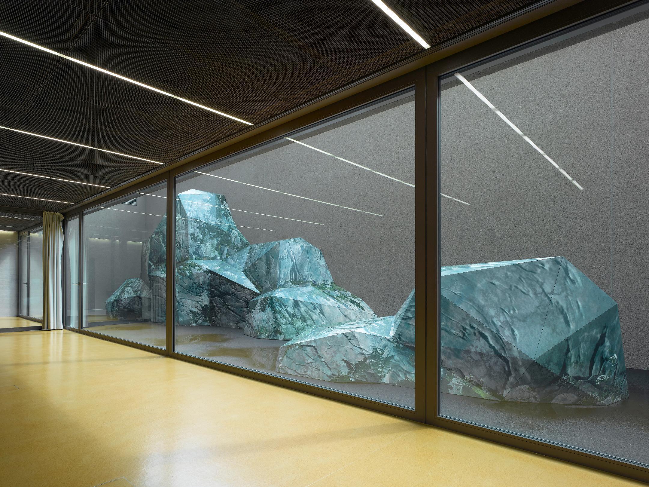 Korridor mit gelbem Boden. Durch das Fenster sieht man Fels-ähnliche Gebilde in Grün.