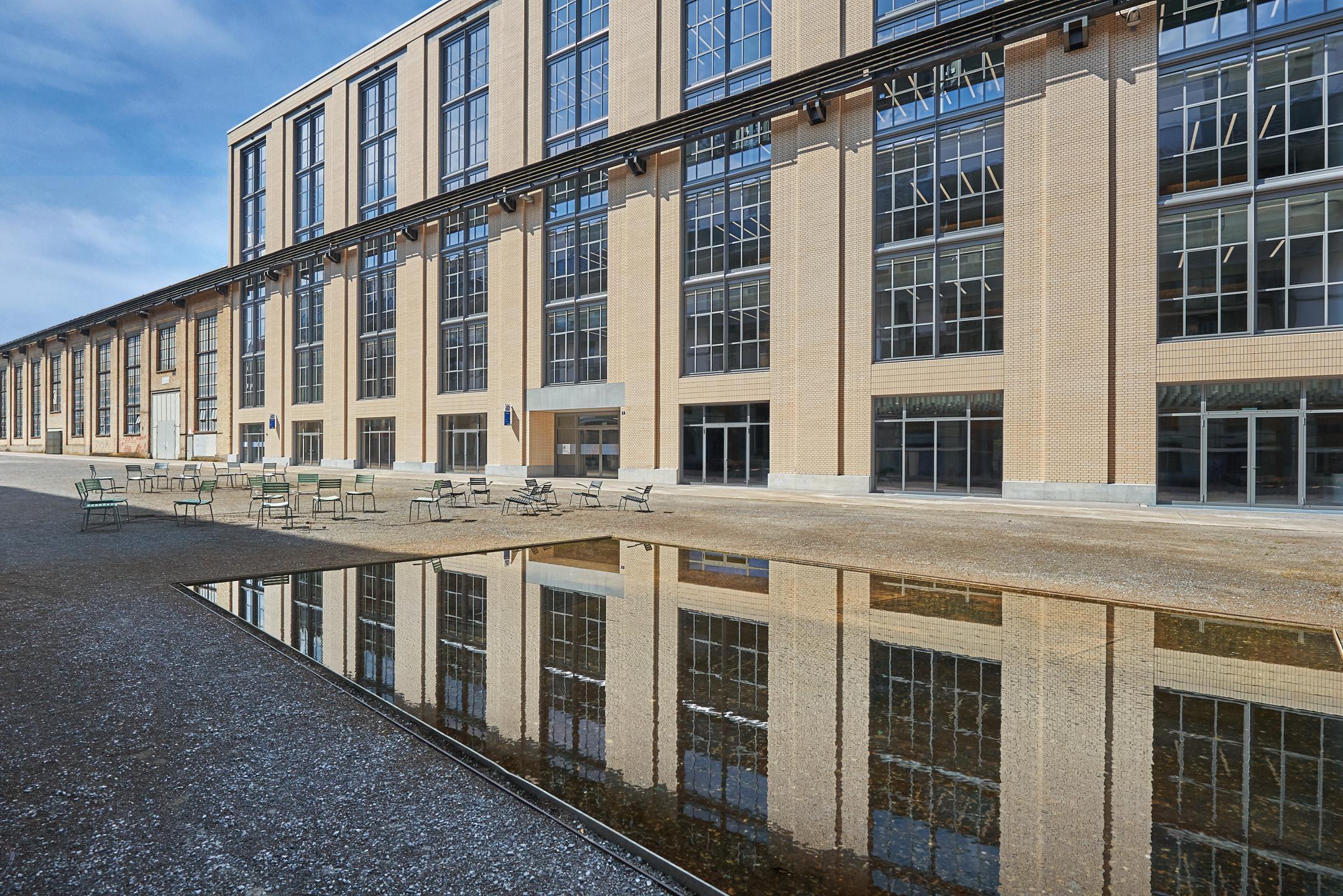 Die mit hellgelben Backsteinen verkleidete Fassade des Neubaus prägt markant den grossflächigen Katharina-Sulzer-Platz. Der industrielle Charakter des Platzes wird durch die an der Fassade erhaltene Kranbahn verstärkt. Als Sitzmöglichkeiten sind in diesem Massstab winzig wirkende Metallstühle auf dem Platz in Gruppen verteilt. Im Vordergrund spiegelt sich die Fassade in der Oberfläche des rechteckigen Wasserbeckens.