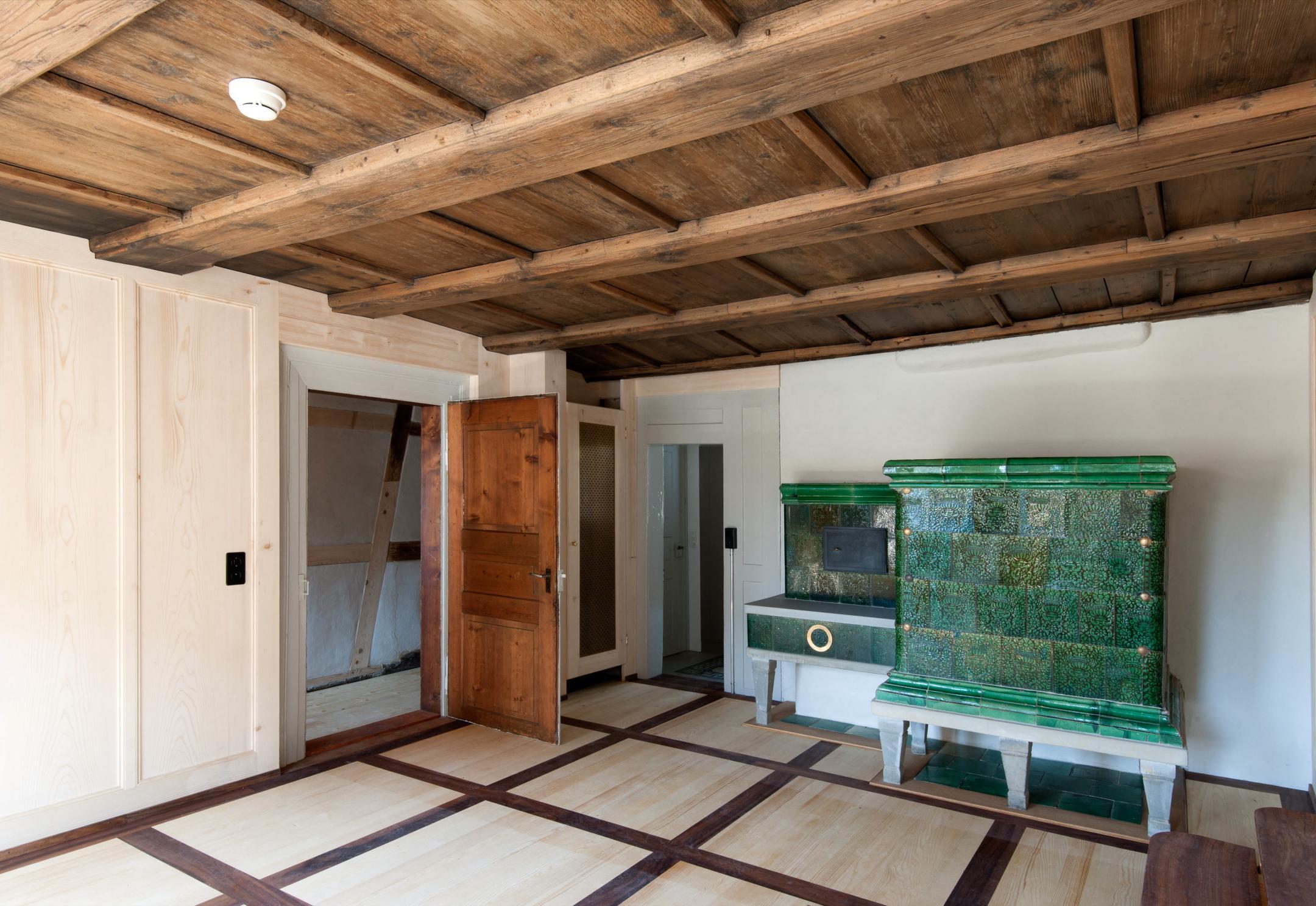 Innenraum in Holz mit alten, restaurierten und neuen Elementen und Kachelofen.