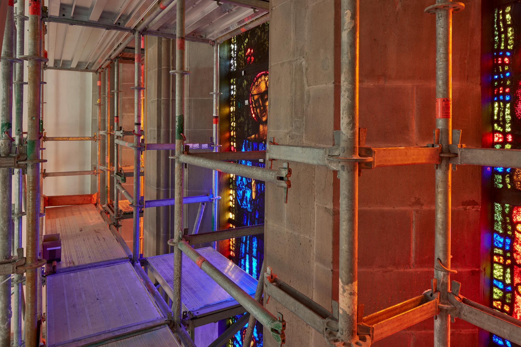 Mauerwerk mit farbigen Fenstern und einem Gerüst.