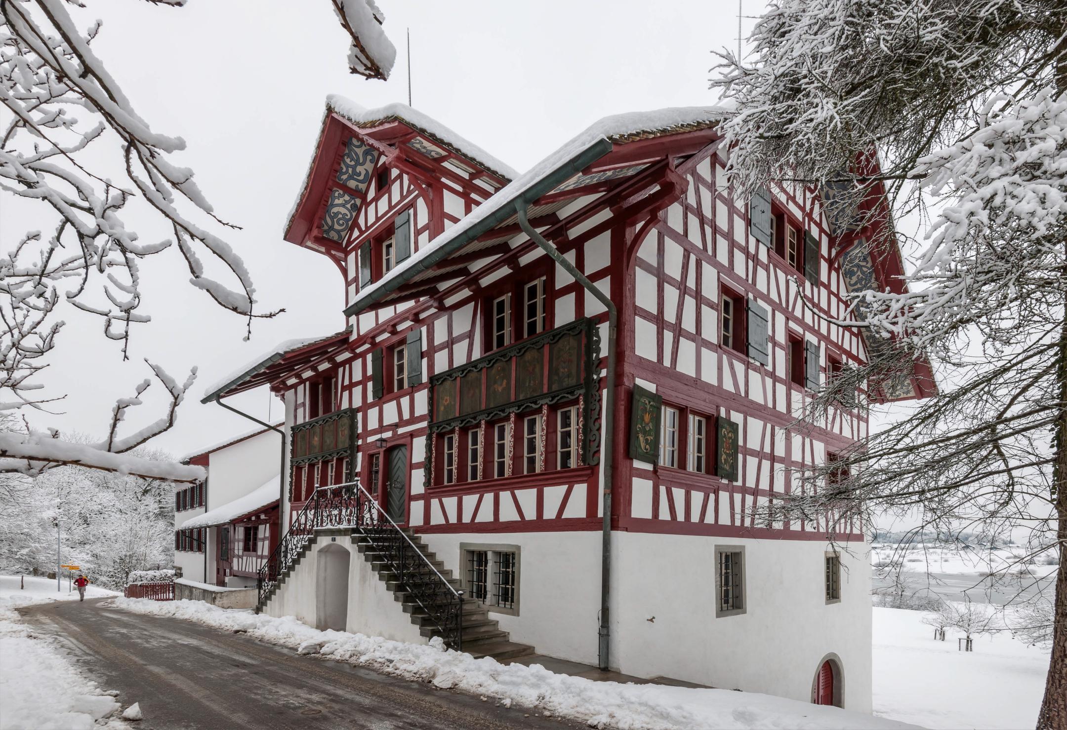 Weisses Gebäude mit roten Holzriegeln in verschneiter Landschaft.