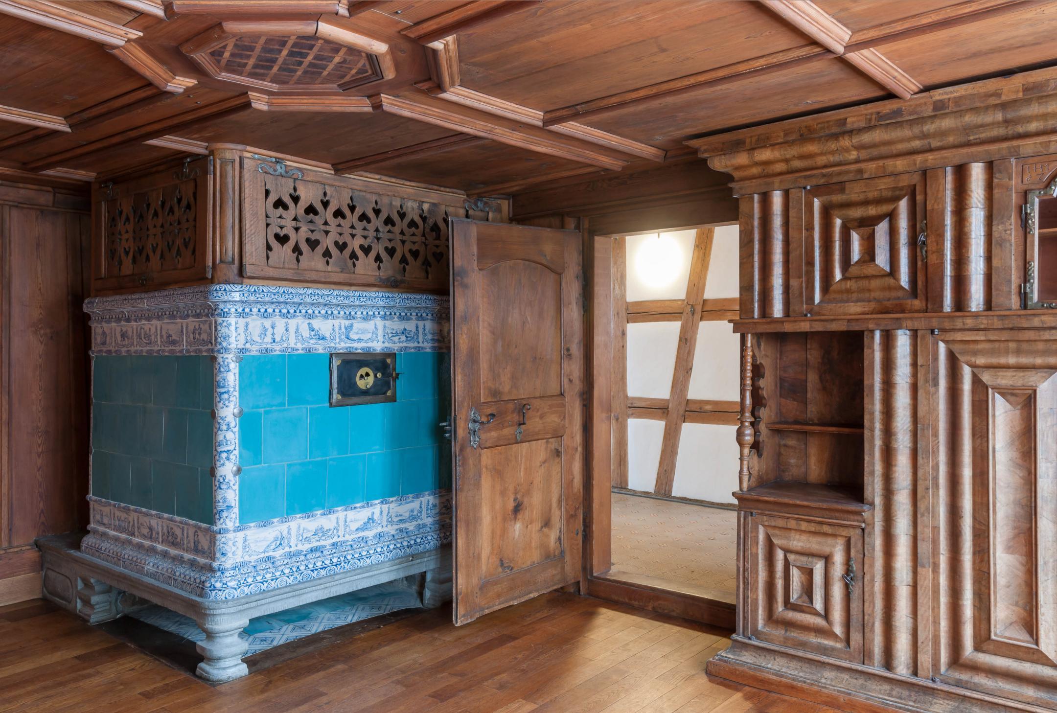 In Sichtholz gehaltener Raum mit grünem Kachelofen.