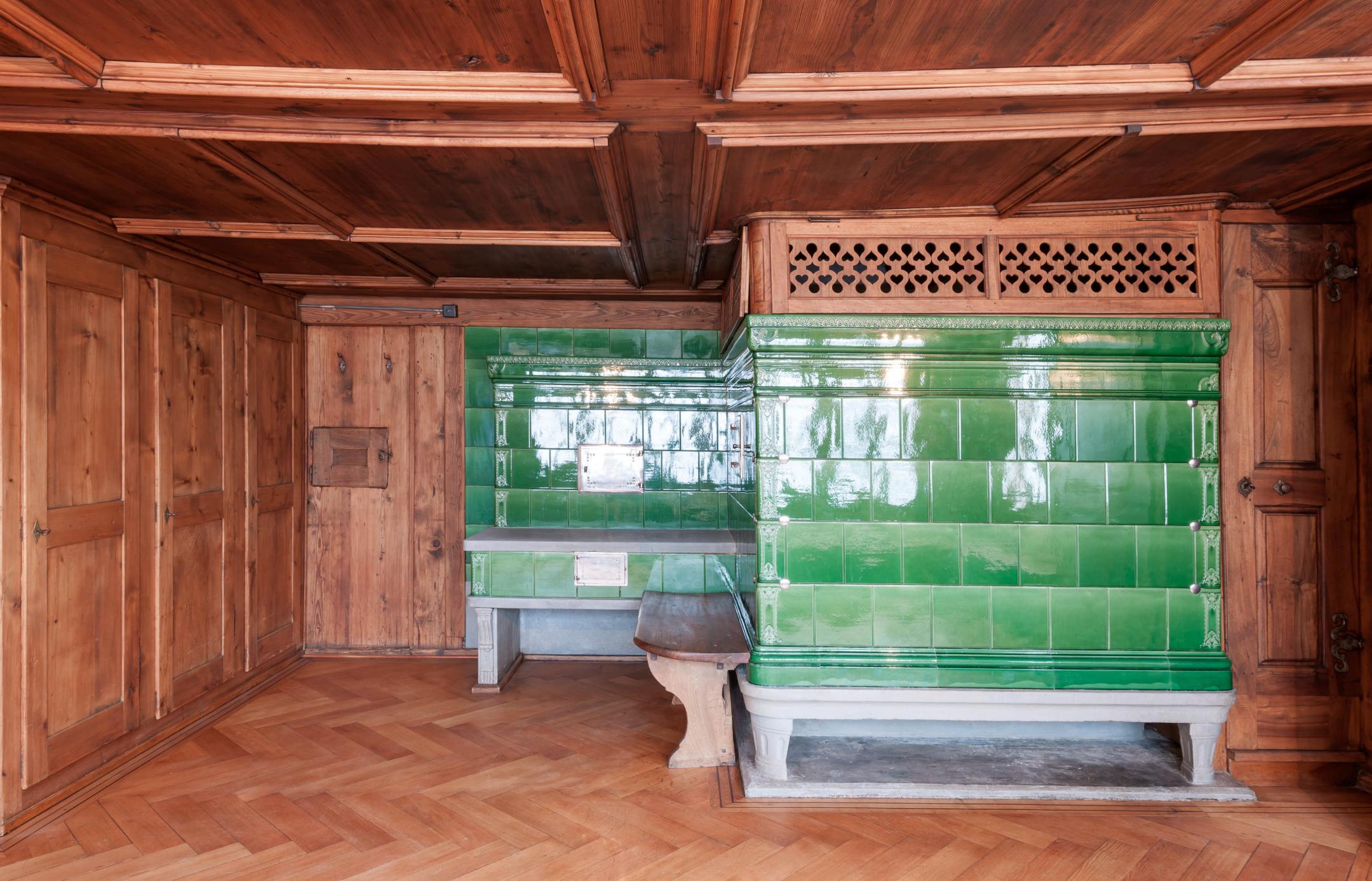 In Sichtholz gehaltener Raum mit grünem Kachelofen.
