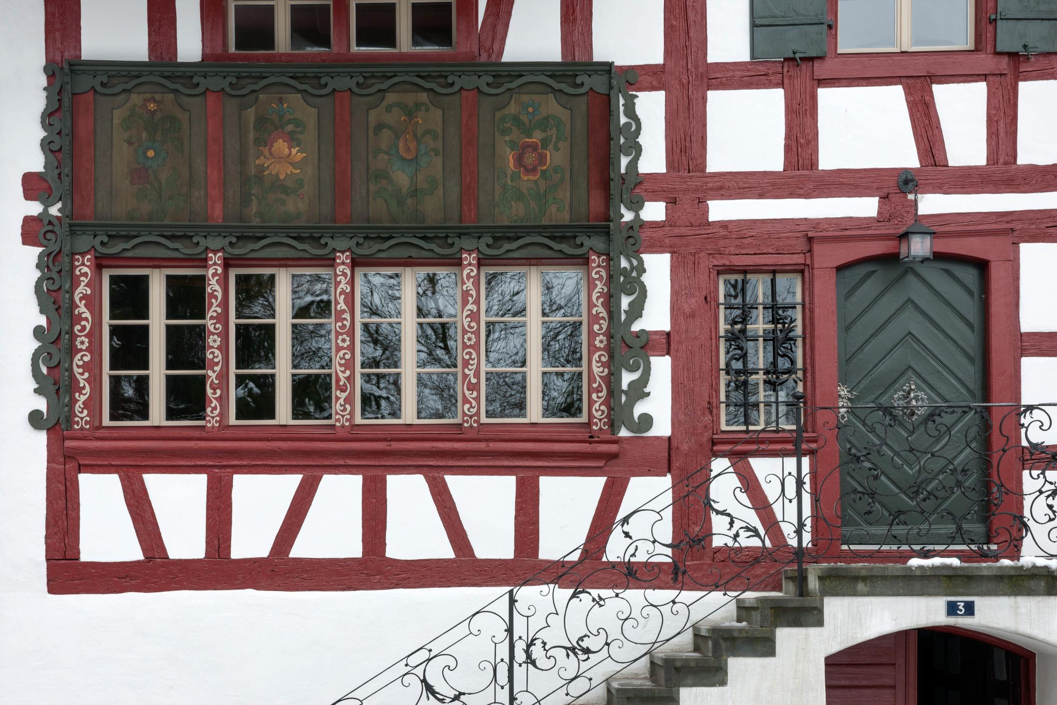 Weisse Fassade mit roten Holzständern. Türe und Fensterläden in grün gestrichenem Holz.