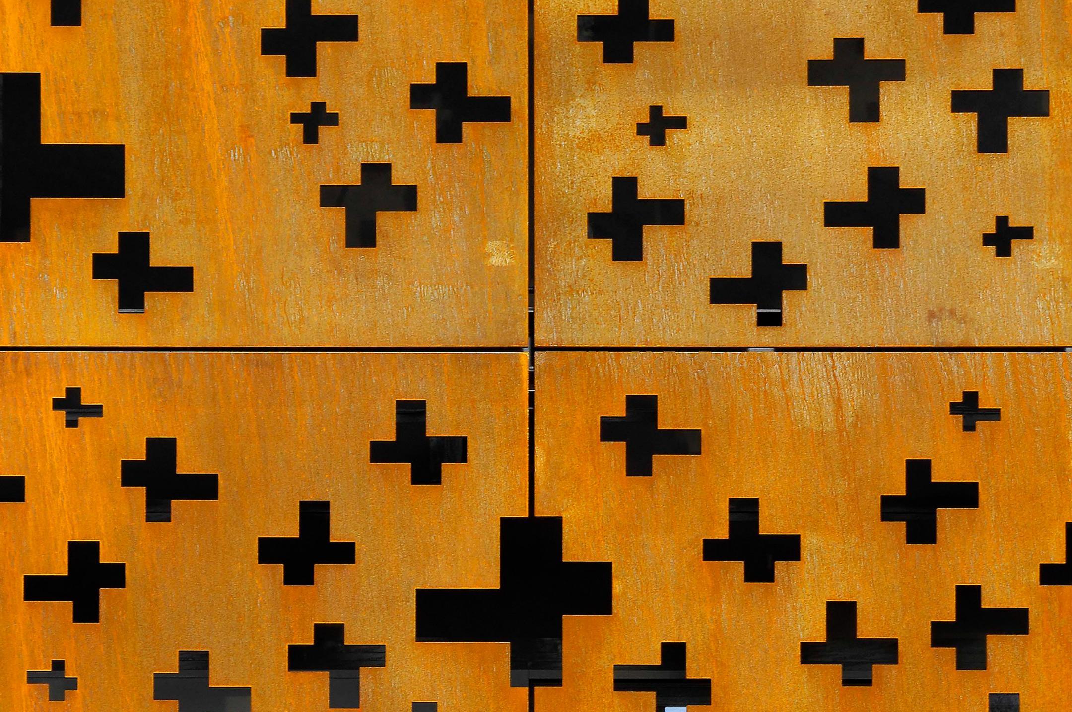 Detailansicht an vier rostige Metallplatten. In die Platten wurden Öffnungen in Form von Kreuzen eingebracht.