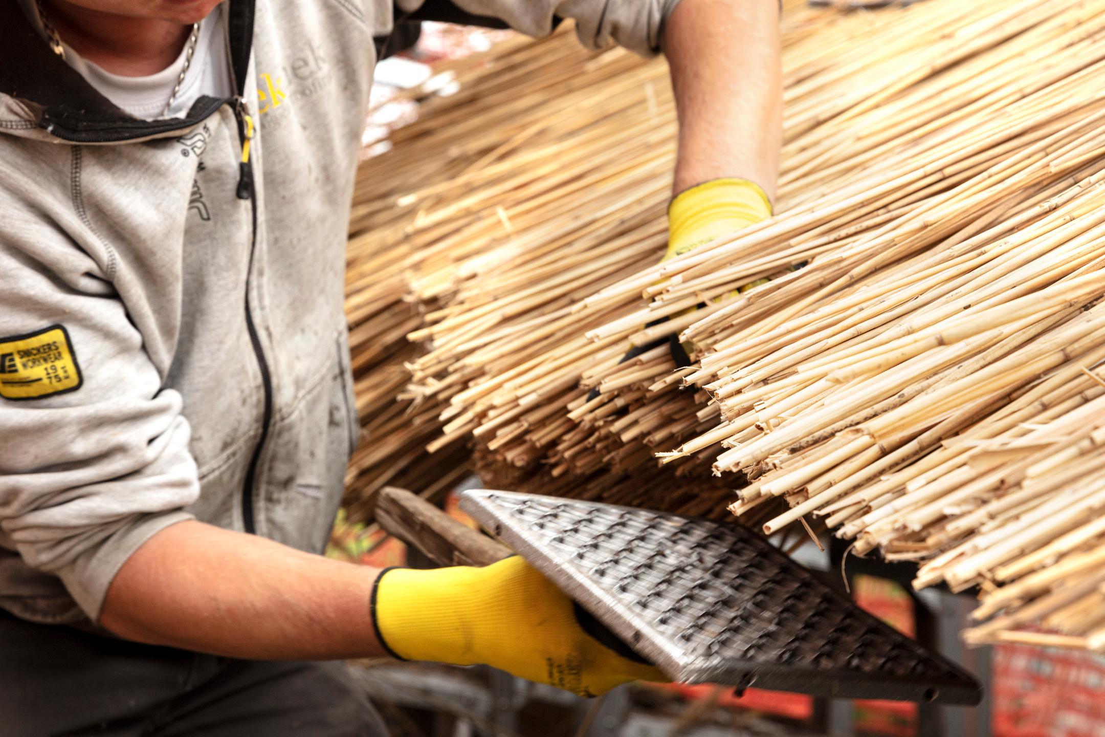 Ein Arbeiter richtet die Schilf-Halme an der Traufe des Daches mit einem «Klapper».