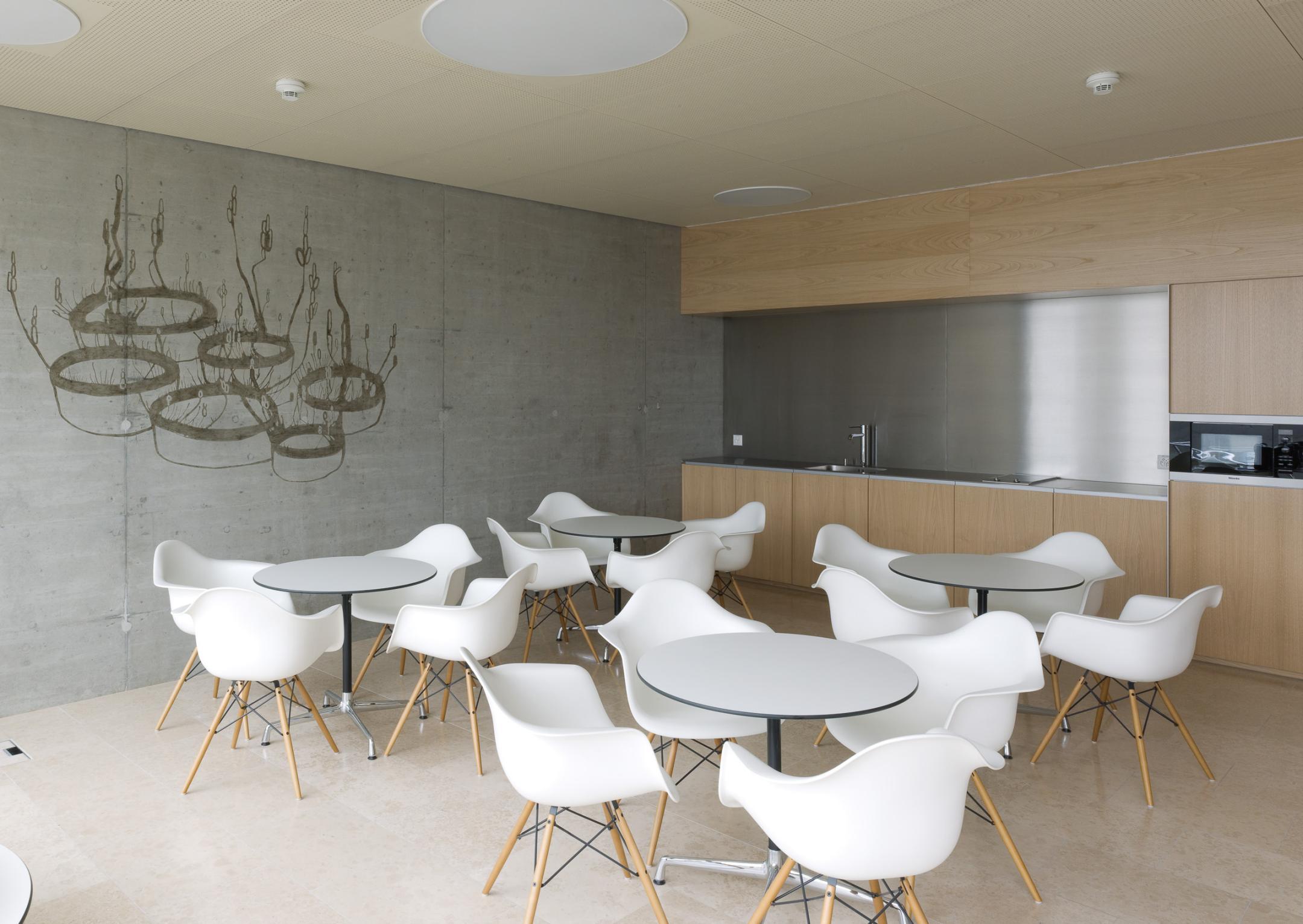 Tischgruppe vor kleiner Küchenzeile. Die Sichtbetonwand ist durch ein Gemälde verziert.