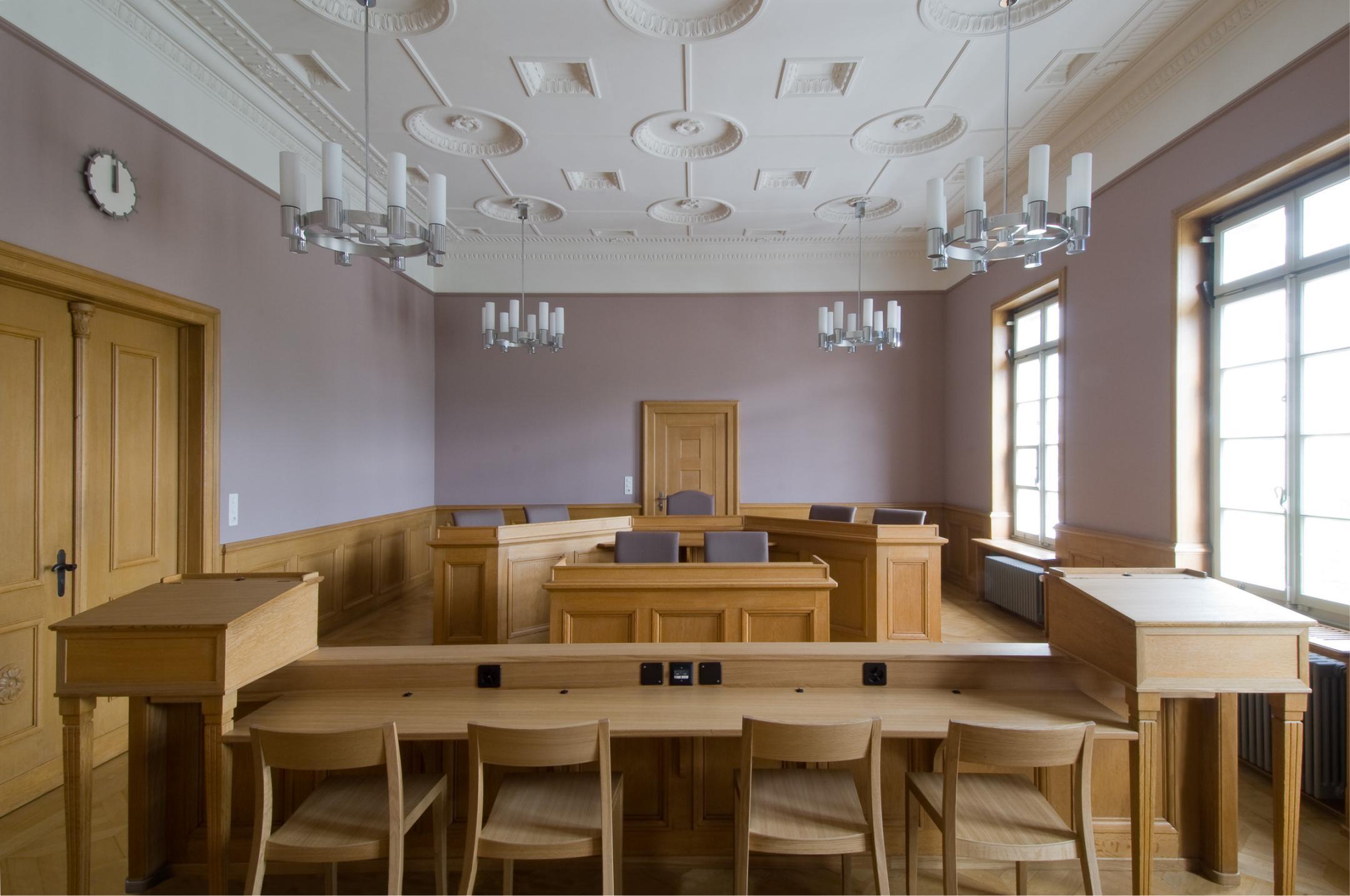 Älterer Raum mit Sitzmöglichkeit für gegenübersitzender Parteien. Die Wände in blassen Farben, die Decke in Weiss und die Einrichtung in Holz