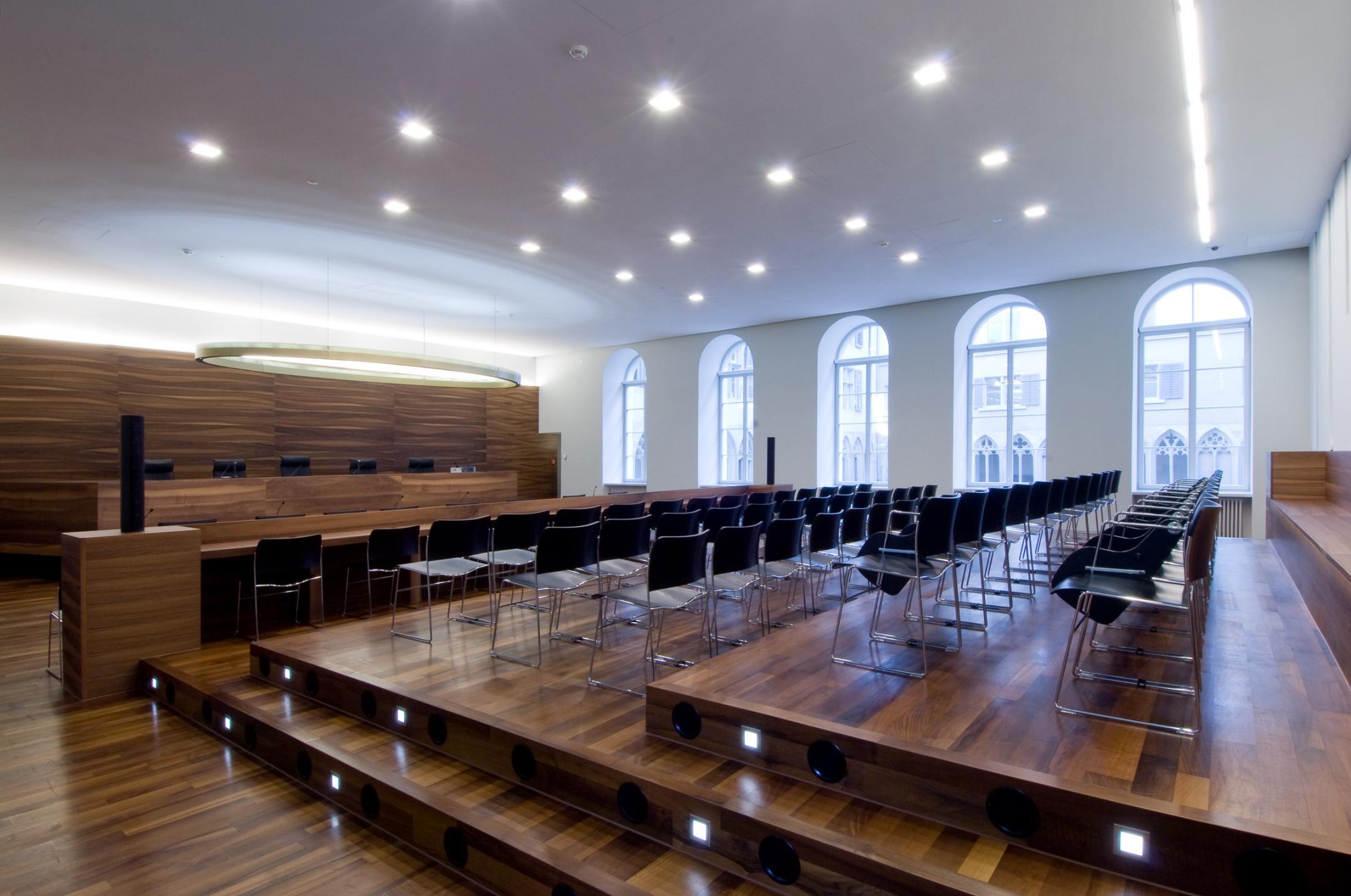 Innenansicht eines grossen Saales mit Podium für das Gericht. Im Saal ist für rund 50 Personen gestuhlt. Der Boden und die Einrichtung sind in dunkllem Holz, die Wände und die Decke in weiss gehalten.