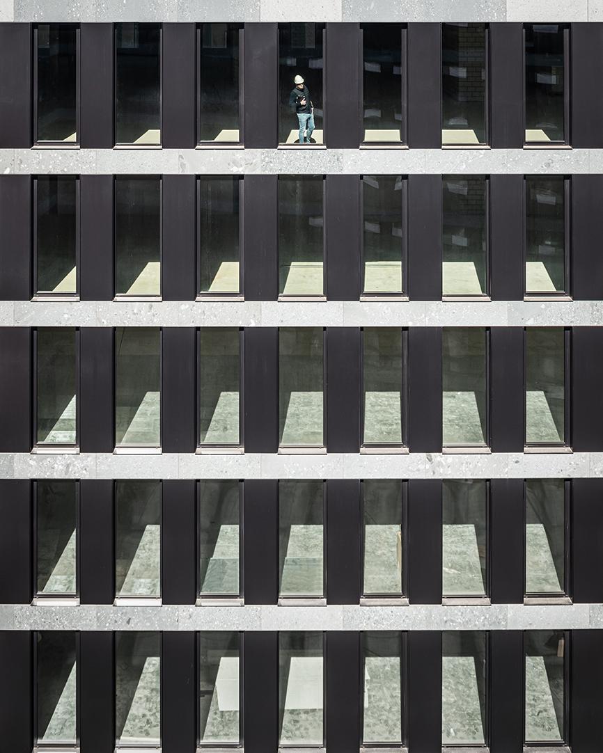 PJZ_Baustelle im April 2020: Zoom auf Fassade mit einem Arbeiter zwischen zwei Fensterrahmen stehend.