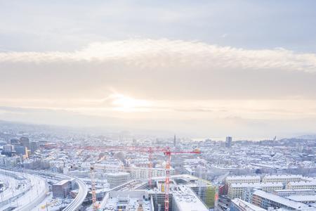 Die verschneite PJZ-Baustelle aus der Höhe aufgenommen, im Hintergrund ist das winterliche Panorama von Zürich sichtbar, bis hin zum Zürichsee. 