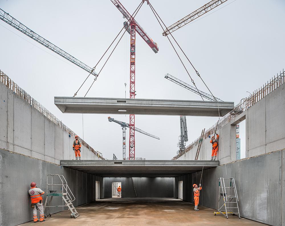 Die PJZ-Baustelle im Februar 2018: Bauarbeiter in oranger Arbeitskleidung und ein am Kran hängendes Bauelement.