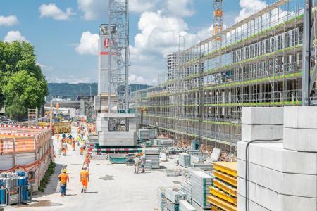 Die PJZ-Baustelle im Juni 2018: Ein in ein Baugerüst verpackter Gebäudeteil, der untere Teil eines Krans, mehrere Bauarbeiter in Arbeitskleidung. 
