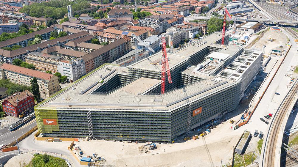Die PJZ-Baustelle im Juni 2019, von schräg oben fotografiert. Das Gebäude ist von einem Baugerüst eingerahmt, zwei rote Kräne ragen daraus hervor.