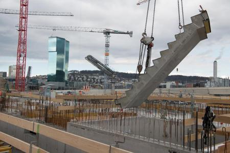Eine Betontreppe schwebt, von Seilen gehalten, über die PJZ-Baustelle im März 2018. Im Hintergrund zwei Kräne und der Primetower. 
