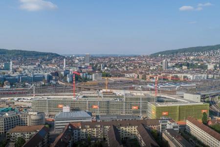 Die PJZ-Baustelle im Mai 2019, aus der Ferne und von schräg oben fotografiert. Im Vordergrund die Häuser der Hohlstrasse, dahinter Bahnschienen und die Stadt.