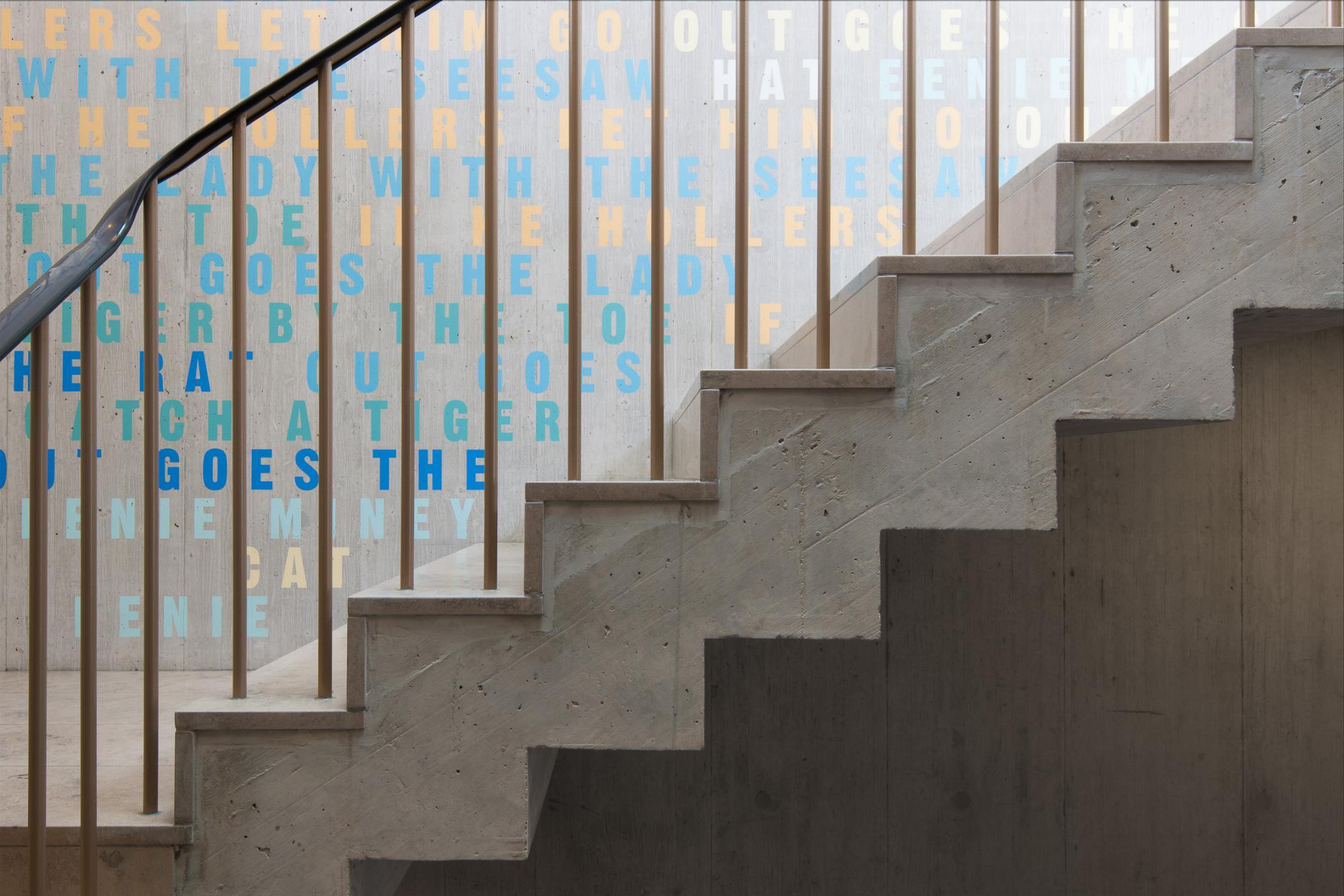 Ansicht an die Treppen im Treppenhaus. Die Wand hinter der Treppe ist mit scheinbar willkürlich gewählten Buchtaben in verschiedenen Farben bemalt.