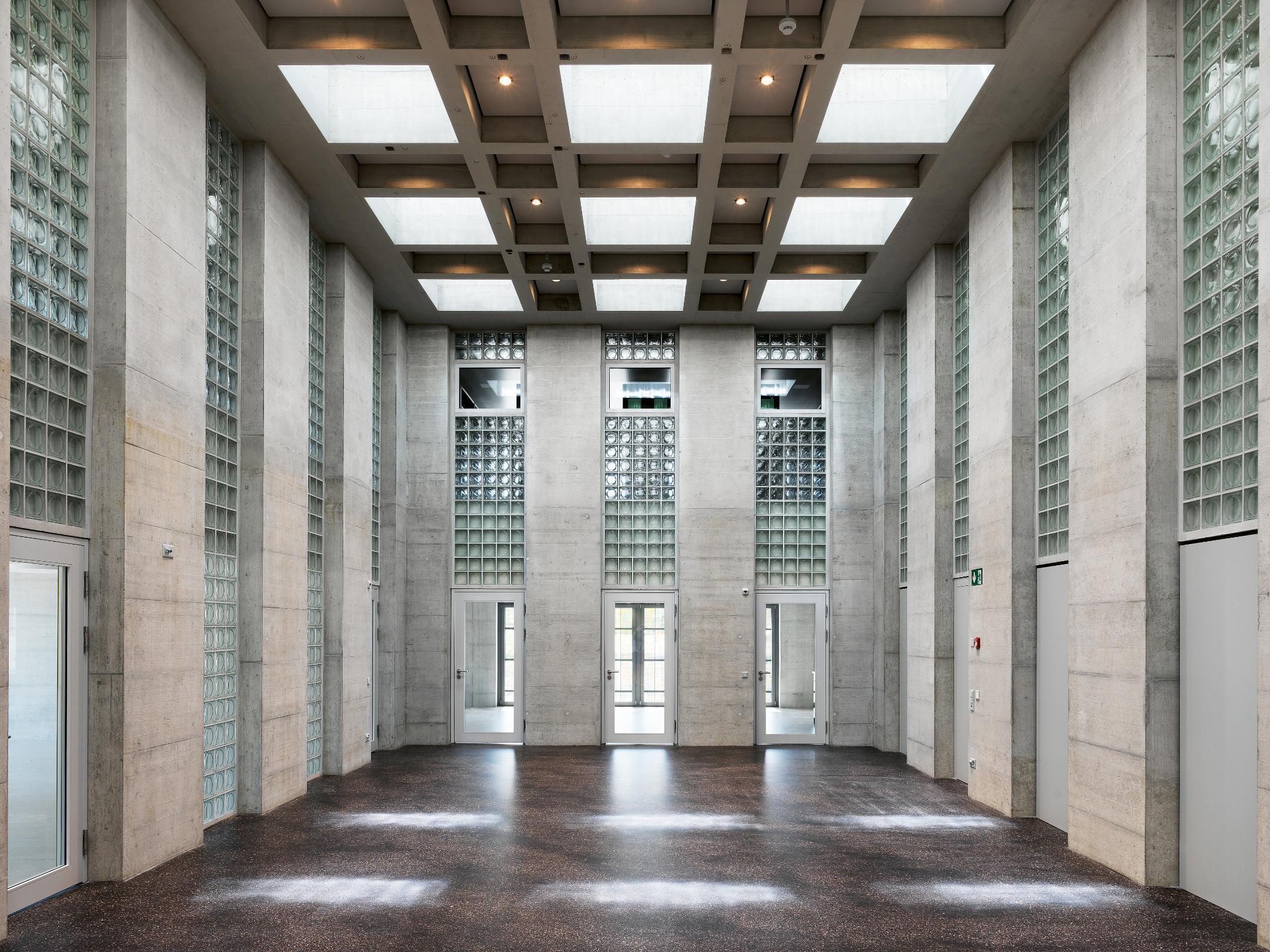 Überhoher Innenraum in Sichtbeton mit grossen Oberlichtern.