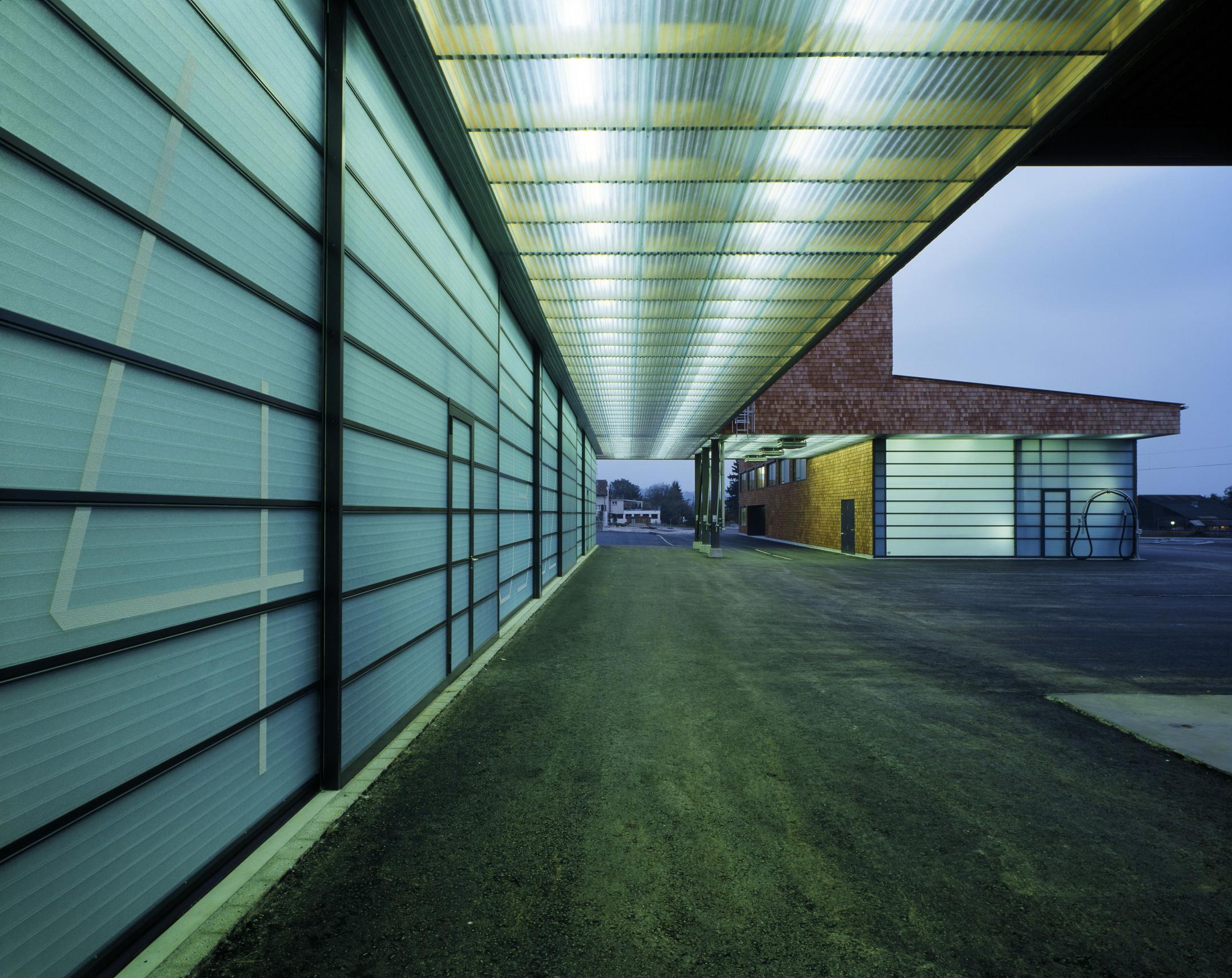 Kantiges Gebäude aus einer überdachten Position aus gesehen. Im unteren Bereich sind grosse Garagentore montiert.