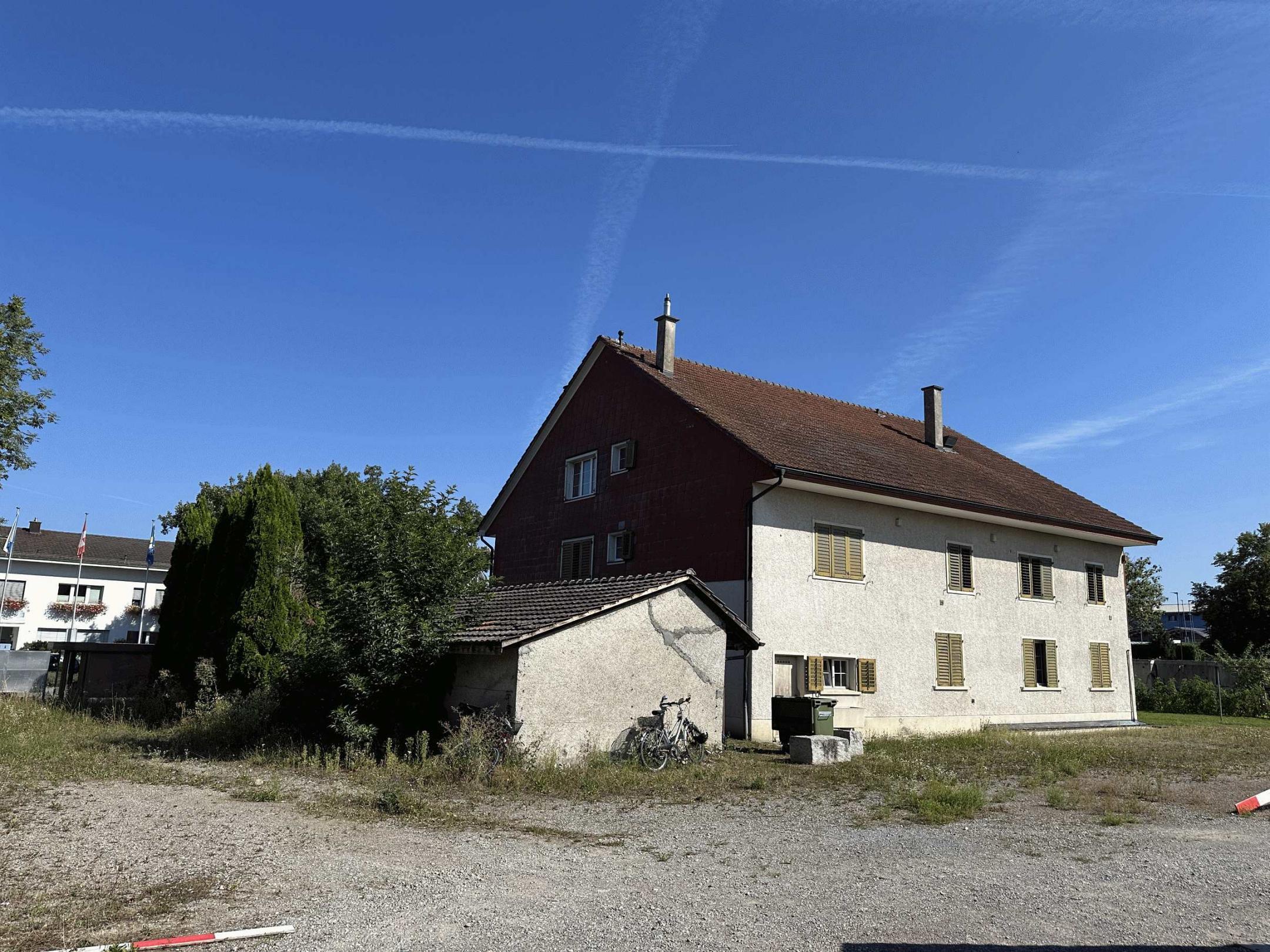 Rückseite Mehrfamilienhaus mit Anbau für Laden und Gebüsch auf der Seite.