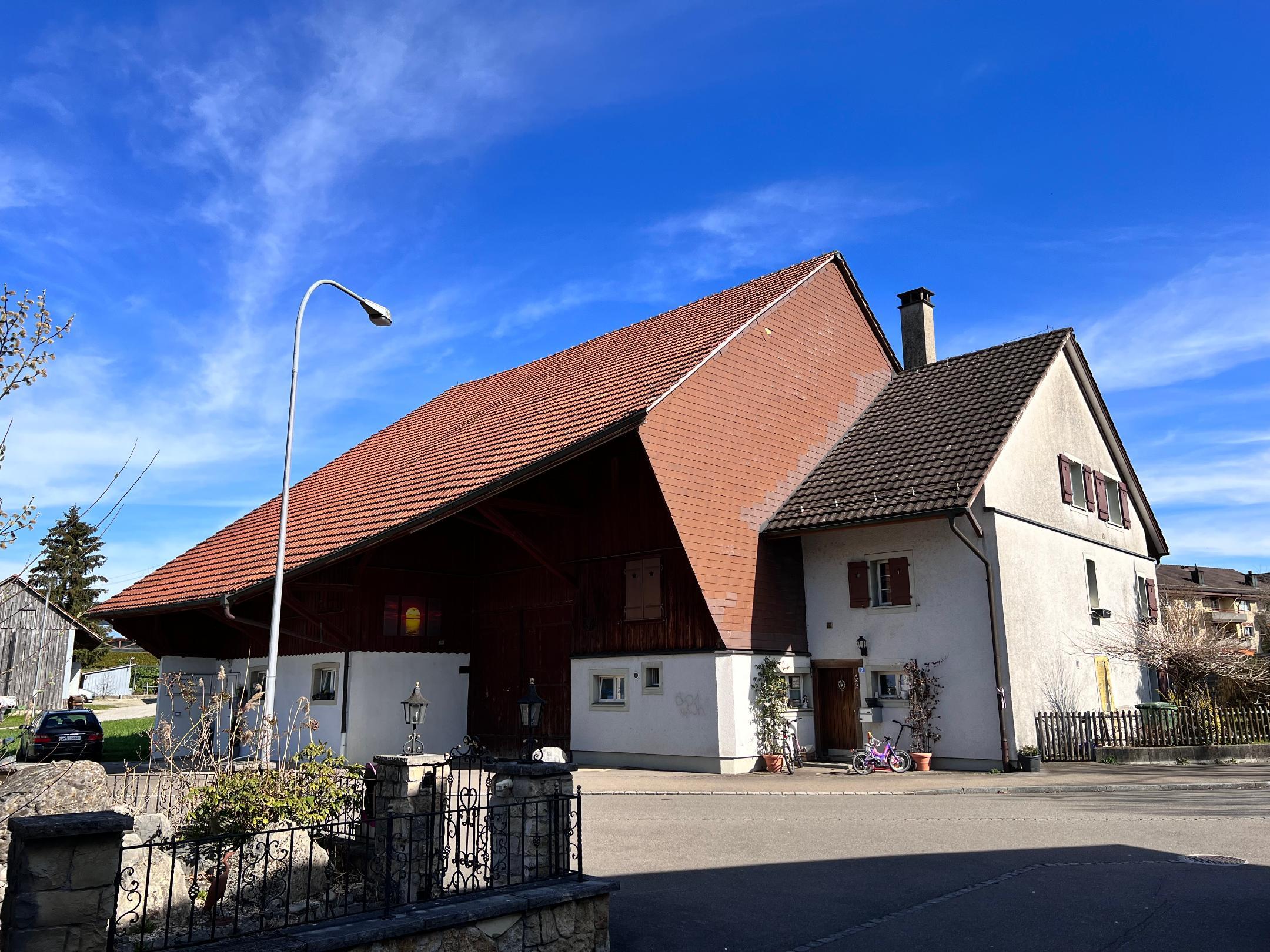 Weisses, dreistöckiges Wohnhaus mit angebauter, grosser Scheune. Die Scheune überragt das Haus deutlich.