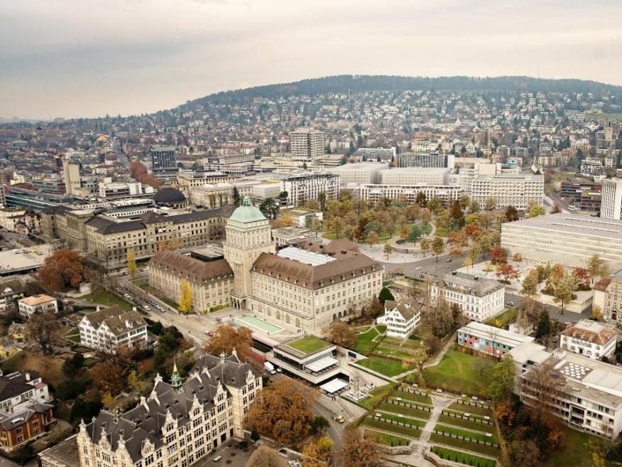 Blick von oben auf das künftige Hochschulgebiet Zürich Zentrum mit der Universität, der ETH und dem Universitätsspital Zürich sowie Grünflächen, im Hintergrund ist der Zürichberg zu sehen.