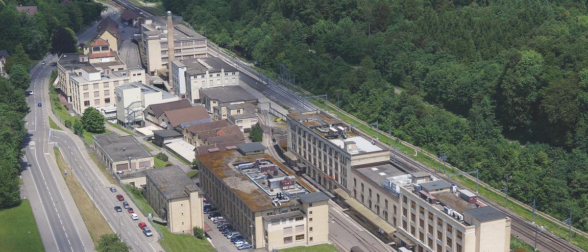 Luftbild von Kemptthal. Die ehemaligen Industriebauten des Maggi-Areals liegen eingebettet in bewaldete Hügel zwischen Kantonsstrasse und Bahnstrecke.
