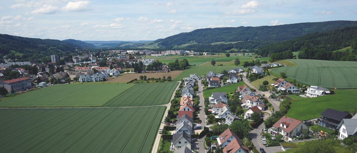 Luftbild mit Blick Richtung Norden auf ein Aussenquartier von Embrach mit Einfamilienhäusern und angrenzendem Ackerland. Links im Hintergrund das Gemeindegebiet von Embrach.