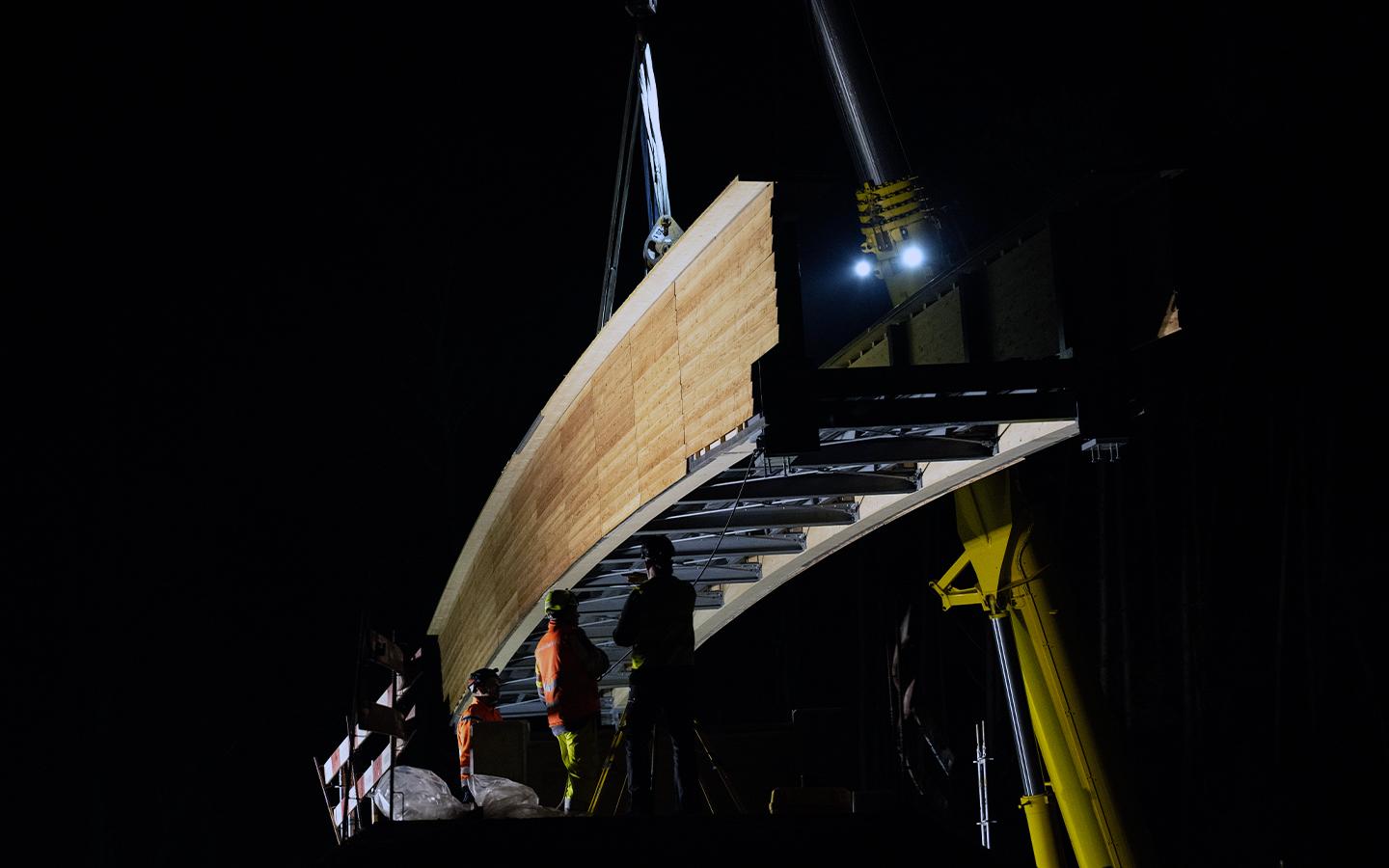 Blick von unten auf die geschwungene Unterseite der Brücke. Die Seitenwände sind mit hellem Holz verkleidet. 