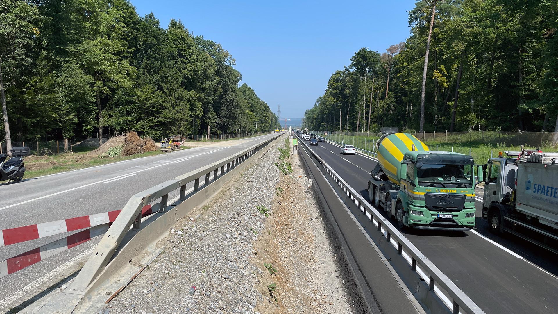 Fahrzeuge fahren auf einer mehrspurigen Strasse, die durch einen Wald führt.