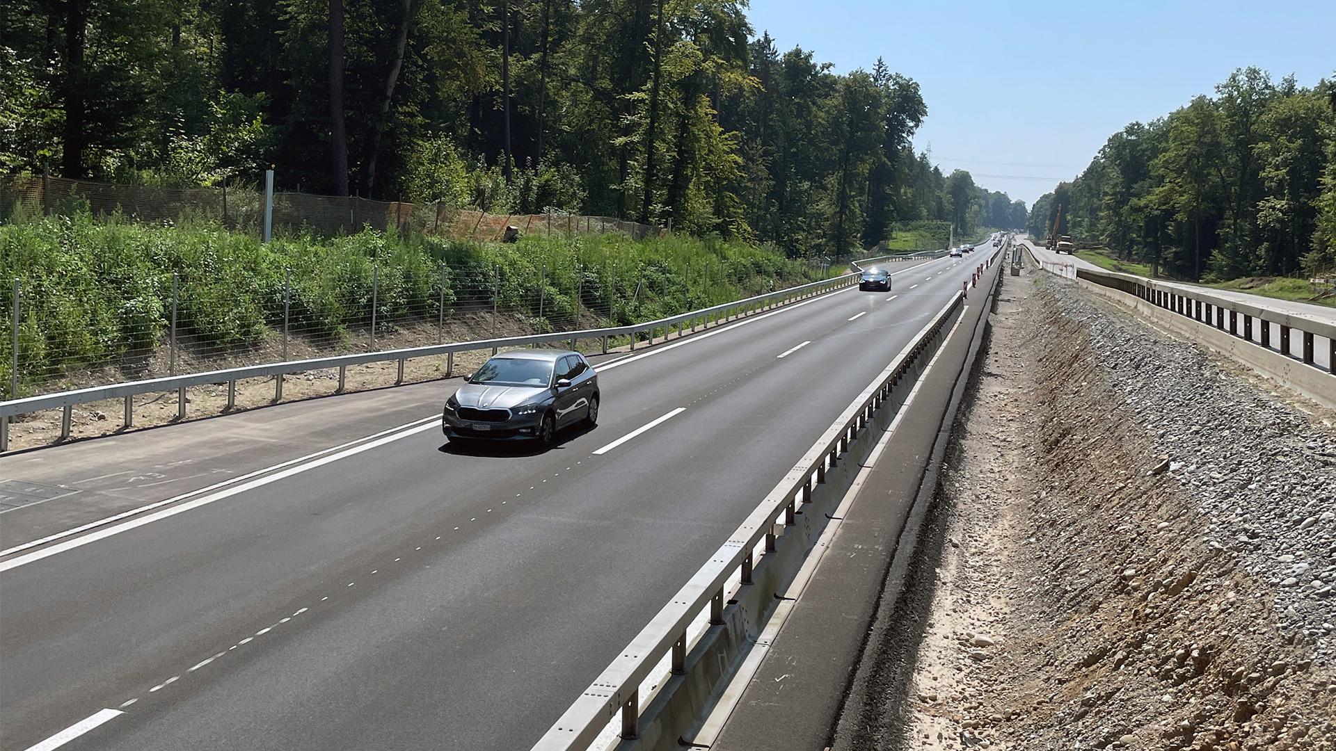 Fahrzeuge fahren auf einer mehrspurigen Strasse, die durch einen Wald führt.