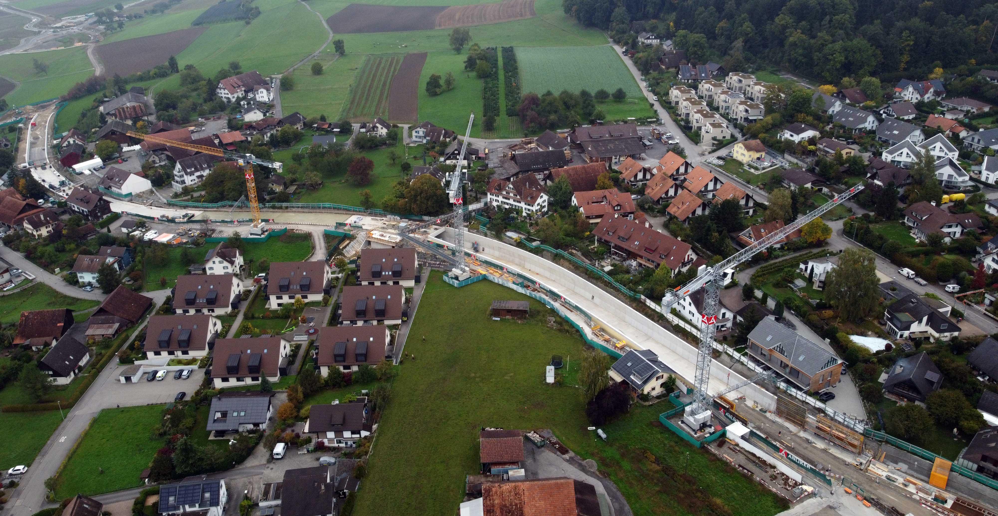 Luftaufnahme der Baustelle mit einer Fussgänger-Passerelle in der Mitte, die die beiden Dorfteile noch bis zum Ende der Bauarbeiten miteinander verbindet.  