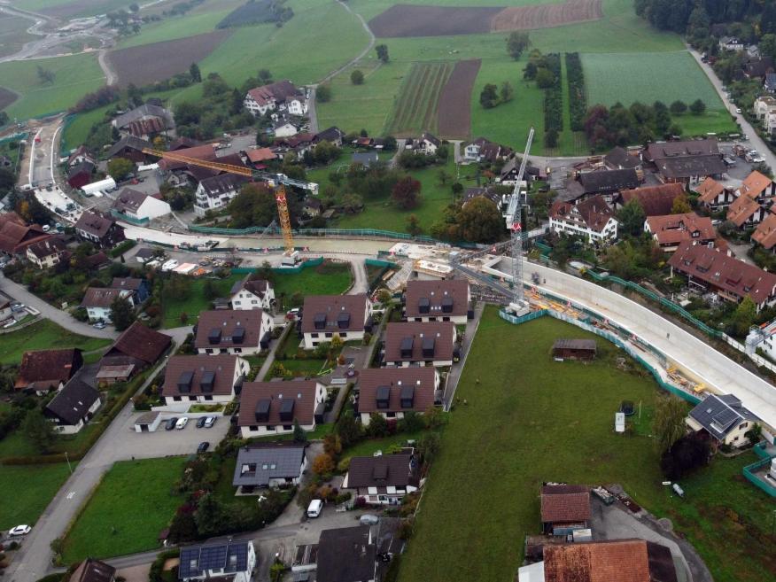 Luftaufnahme der Baustelle mit einer Fussgänger-Passerelle in der Mitte, die die beiden Dorfteile noch bis zum Ende der Bauarbeiten miteinander verbindet.  