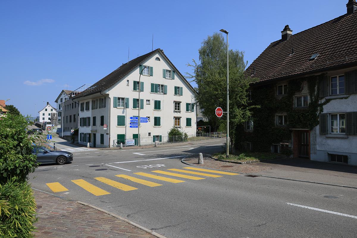Eine Strassenkreuzung mit gelbem Fussgängerstreifen, Stopp-Schild und traditionellen Wohnhäusern.