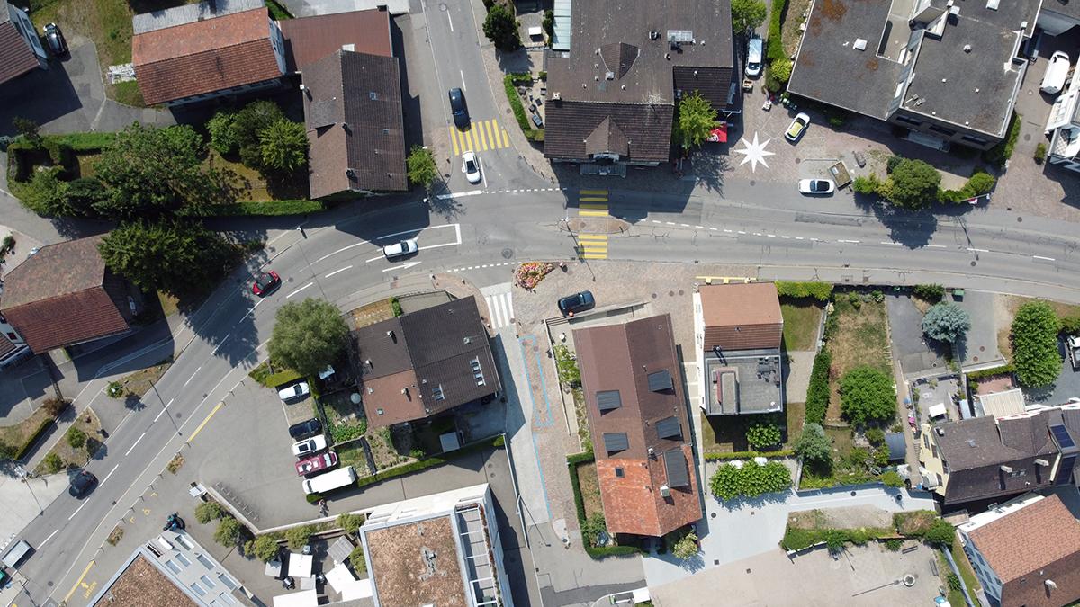Drohnen-Luftaufnahme von oben auf eine Strassenkreuzung, Dächer von Wohnhäusern und Parkplätze.