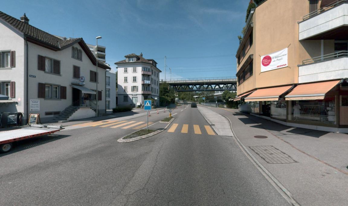 Strasse mit einem Fussgängerübergang mit Mittelschutzinsel durch Häuser.