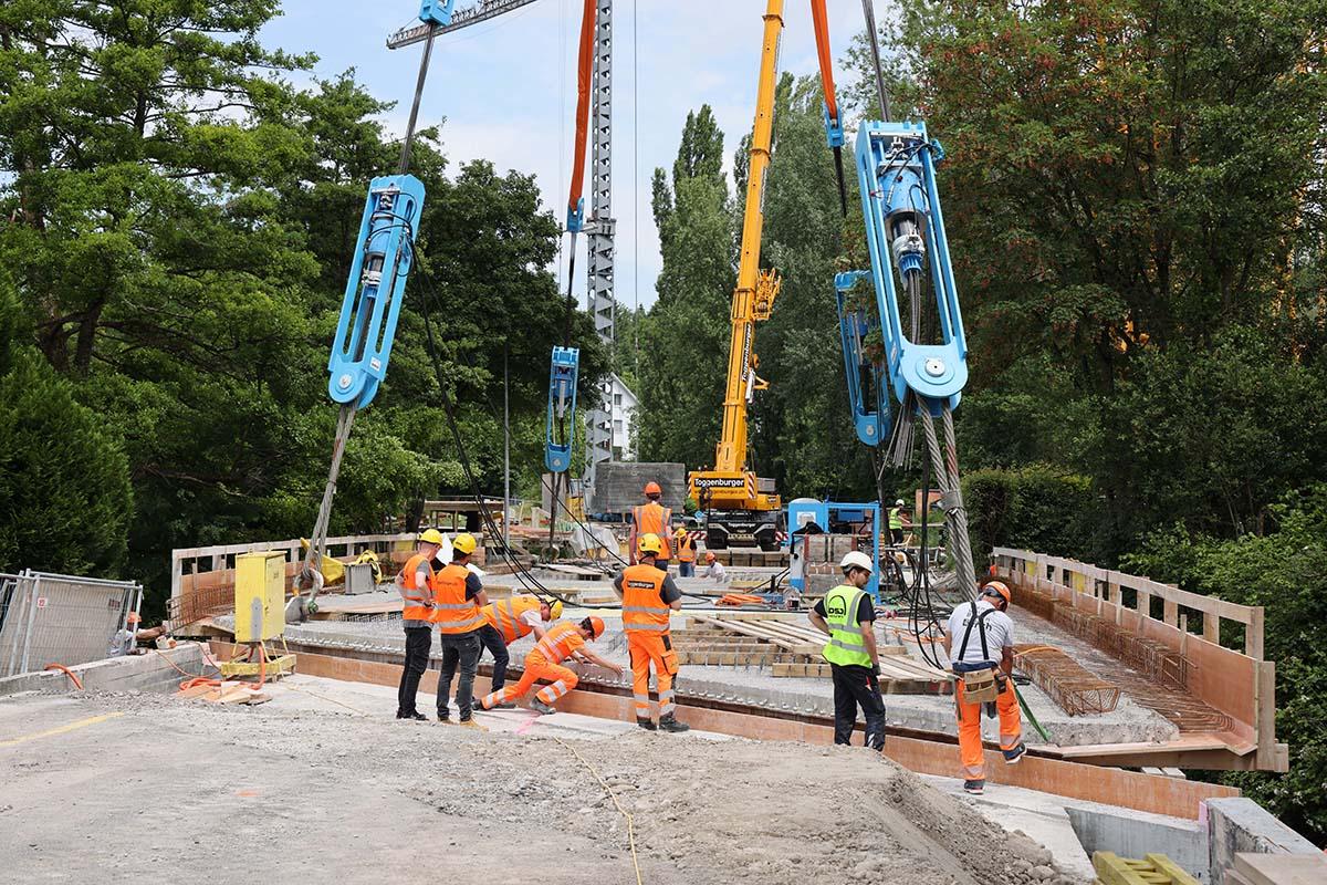 Bauleute in Leuchtwesten und eine Brücke die an vier Seilen hängt