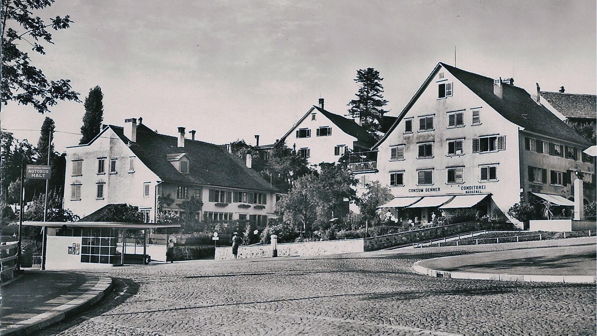 Historische Schwarz-Weiss-Aufnahme des Dufourkreisels mit alten Häusern, Kopfsteinpflaster und einer Bushaltestelle.