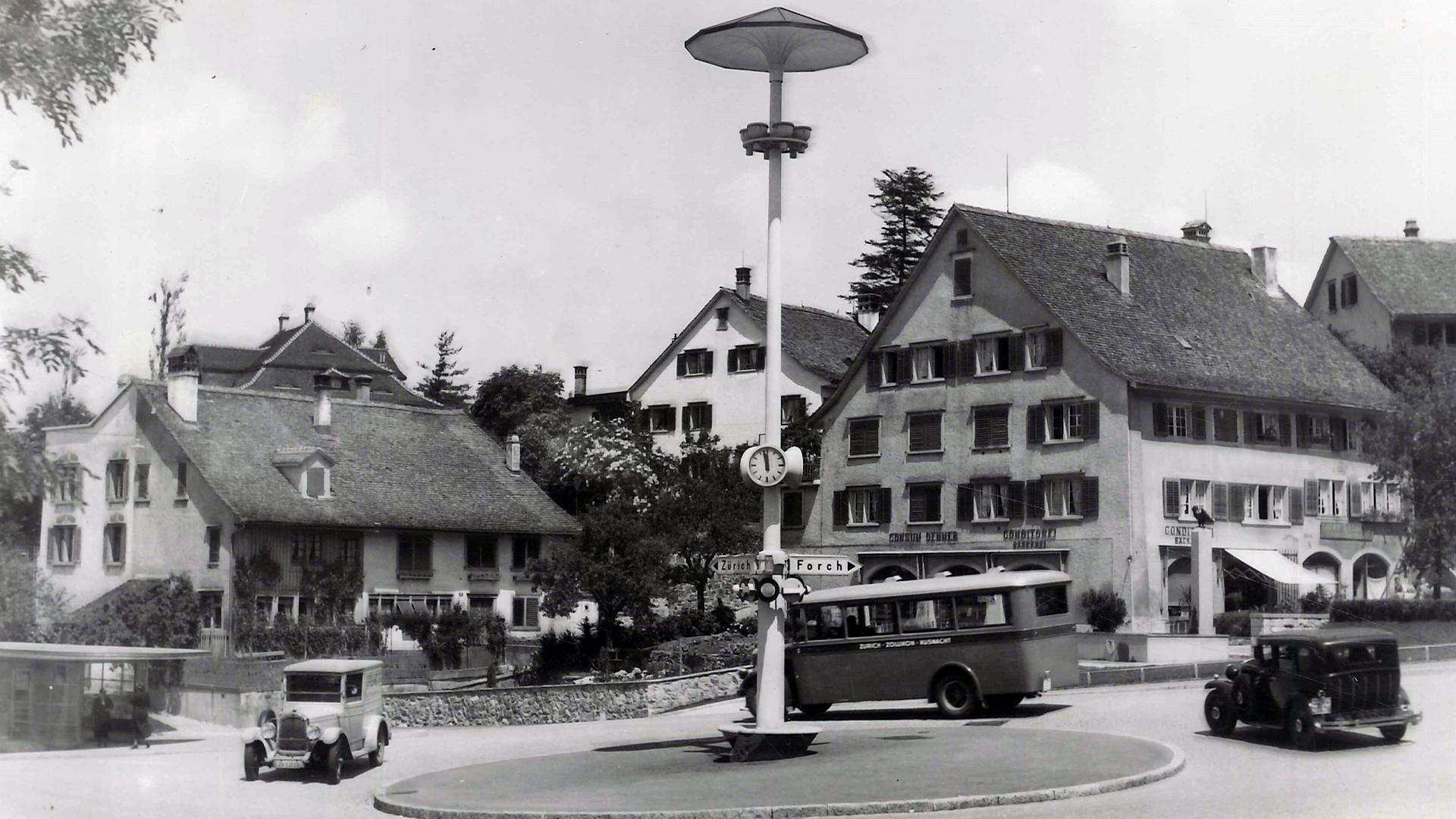Historische Schwarz-Weiss-Aufnahme des Dufourkreisels mit einem alten Bus, Autos und der zentralen Kreiselbeleuchtung.