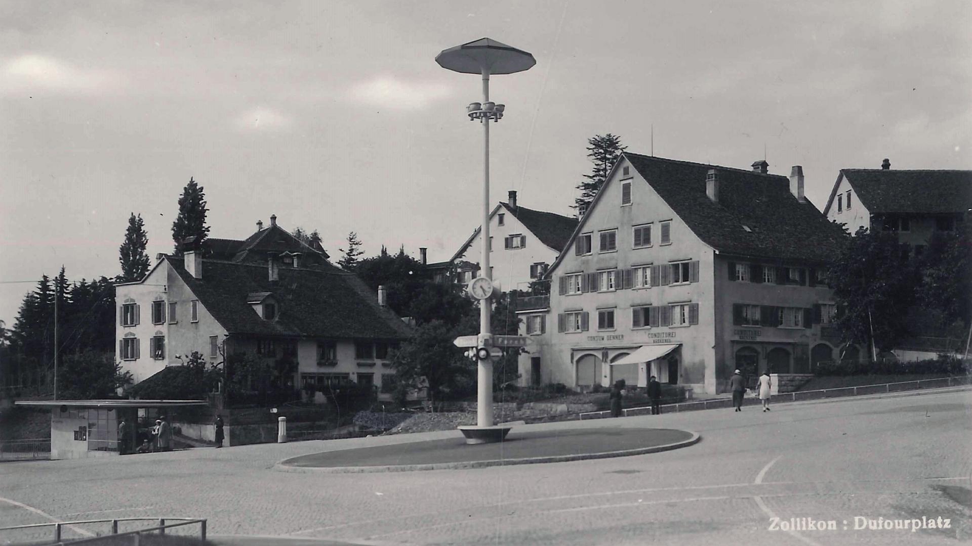Historische Schwarz-Weiss-Aufnahme des Dufourplatzes mit Kopfsteinpflaster, der zentralen Beleuchtungssäule und umliegenden Gebäuden.