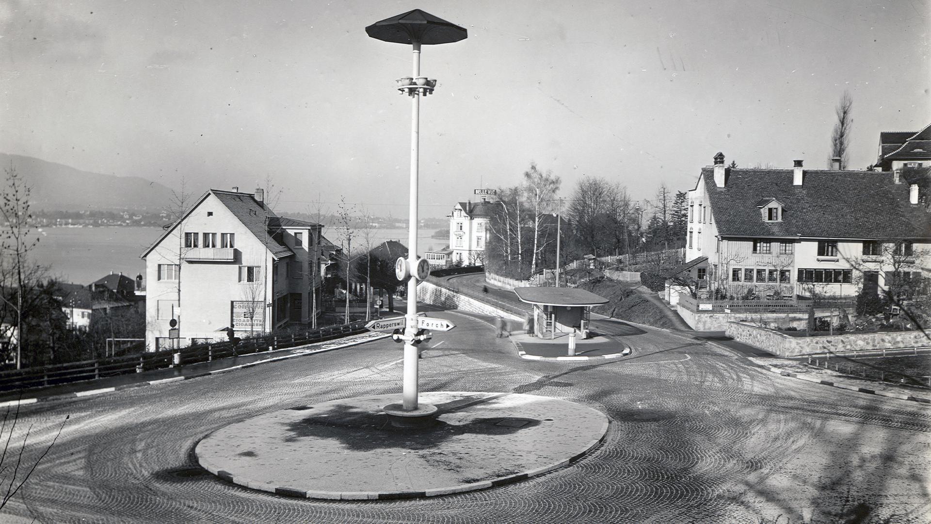 Historische Schwarz-Weiss-Aufnahme des Dufourkreisels mit Tankstelle, zentraler Säule und dem Zürichsee im Hintergrund. Im Hintergrund ist die breite Fläche des Zürichsees sichtbar.
