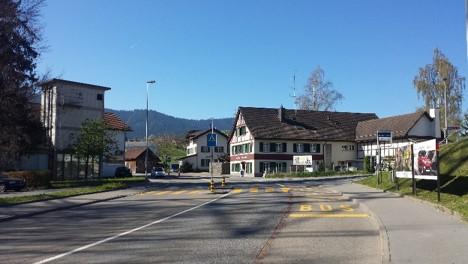 Das Foto zeigt die heutige Situation an der Bergstrasse in Richterswil. Sichtbar sind zwei Autospuren und eine Busspur; ein Fussgängerstreifen kreuzt die Fahrbahnen. Im Hintergrund mehrere Häuser. 