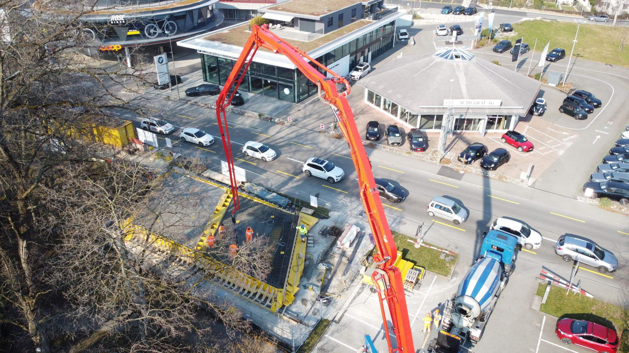 Seitlich von oben fotografierte Baustelle an der Seestrasse in Meilen mit rotem Kran und blauweissem Fahrmischer.  